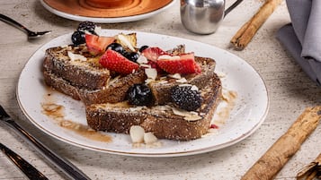 A plate of French toast with strawberries, blackberries, and almonds, accompanied by a cup and a spoon on a wooden table.