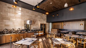 A modern restaurant with wooden flooring, brick walls, and a mix of wooden and metal furniture. - TRYP by Wyndham San Luis Potosi Hotel & Suites (San Luis Potosi)