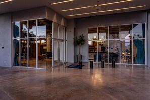 Un vestíbulo amplio con piso de concreto pulido, puertas de vidrio grandes que dan a un área de descanso y un diseño de techo moderno con iluminación lineal.
