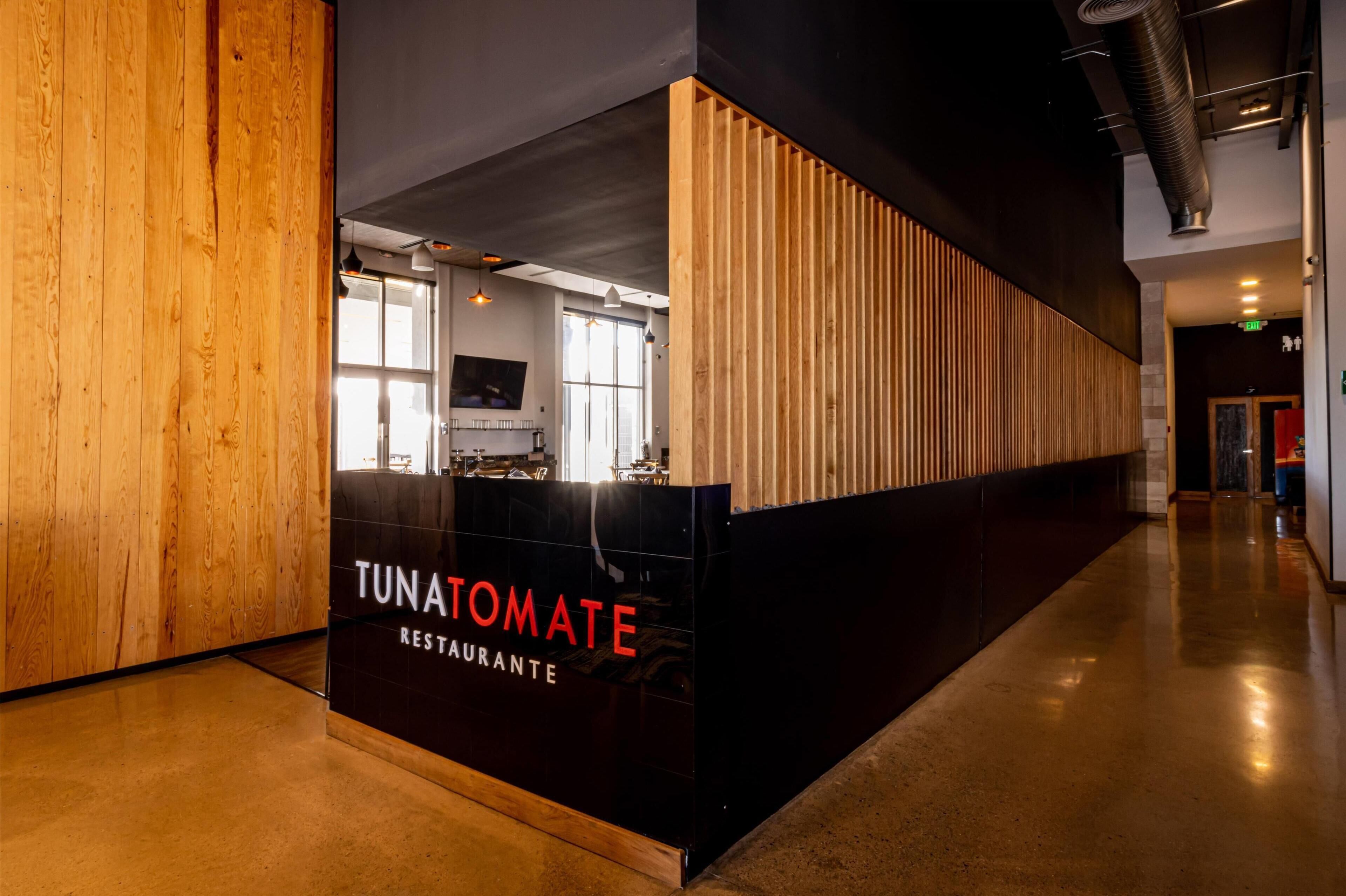 A modern interior with a reception desk labeled "TUNATOMATE RESTAURANTE" and a wooden panel wall.