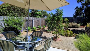 A patio with a glass table and chairs, a beige umbrella, and a variety of potted plants.