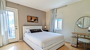 A bedroom with a bed, a desk, a chair, a lamp, and a painting on the wall.