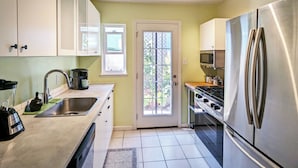 A kitchen with white cabinets, a stainless steel refrigerator, a microwave, a stove, and a coffee maker.