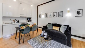 Um espaço de estar moderno com área de jantar, cozinha e um sofá de couro preto com almofadas.