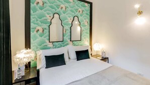 Quarto com cama, duas mesinhas de cabeceira, espelho fixado na parede e parede decorativa com padrão de nuvens.