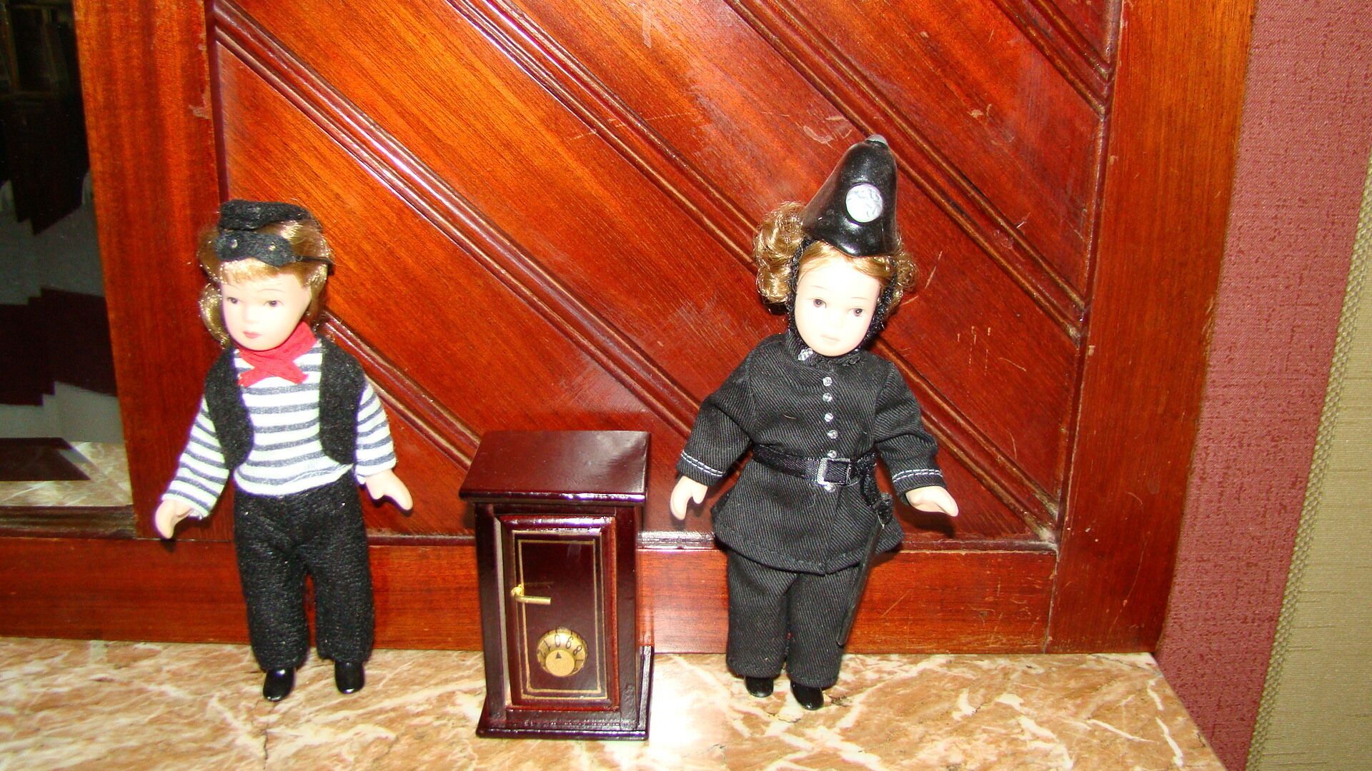 Two dolls standing next to a small wooden box with a lock.