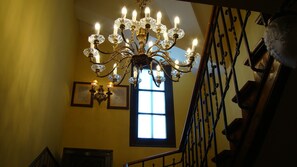 A grand chandelier with multiple lights, a staircase with ornate metal railings, and a window with natural light. - PIEDRAHÍTA RURAL HOUSE (ART DÈCO) (Piedrahíta)