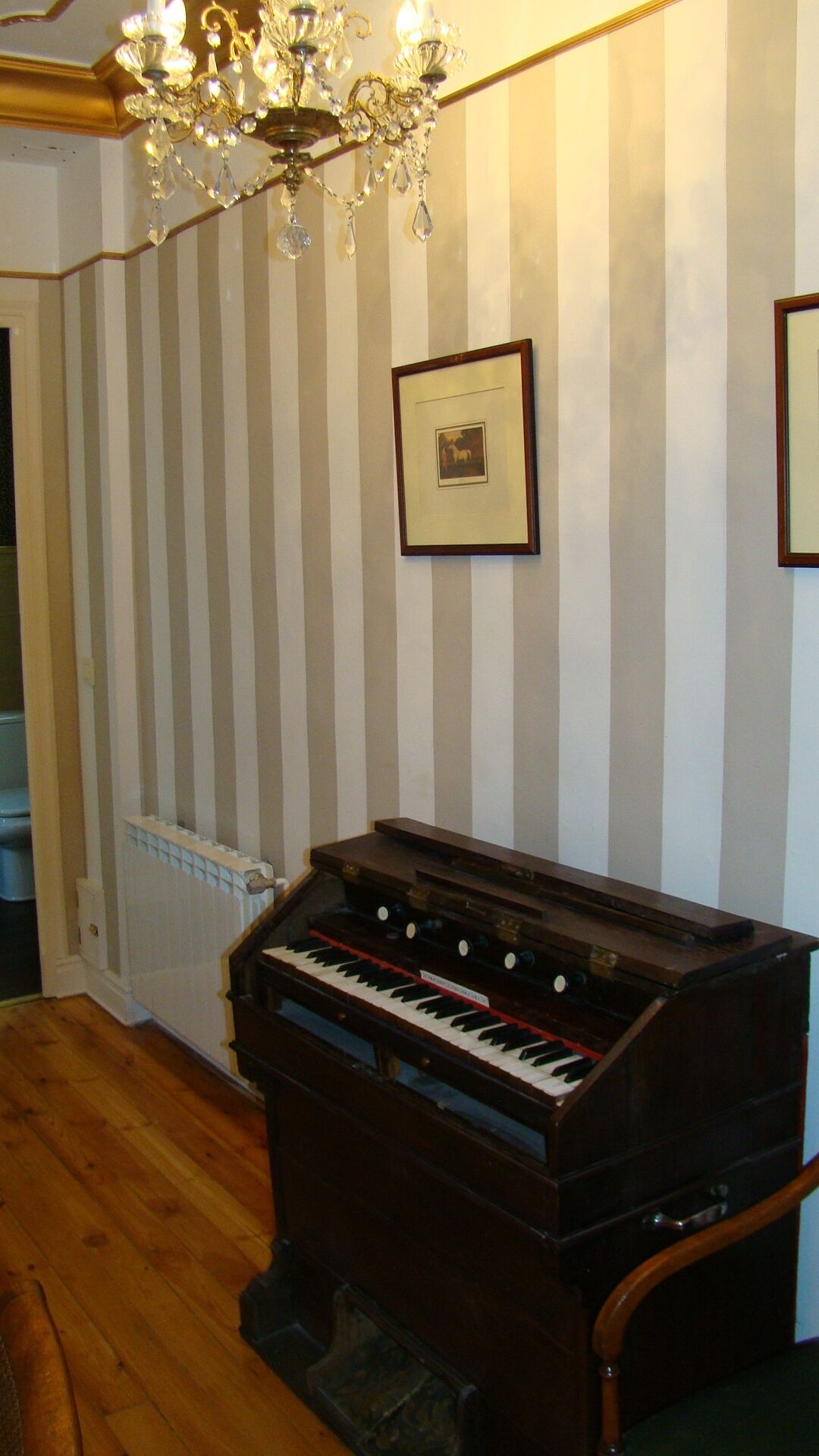 Una habitación con un piano, una araña y papel tapiz a rayas.
