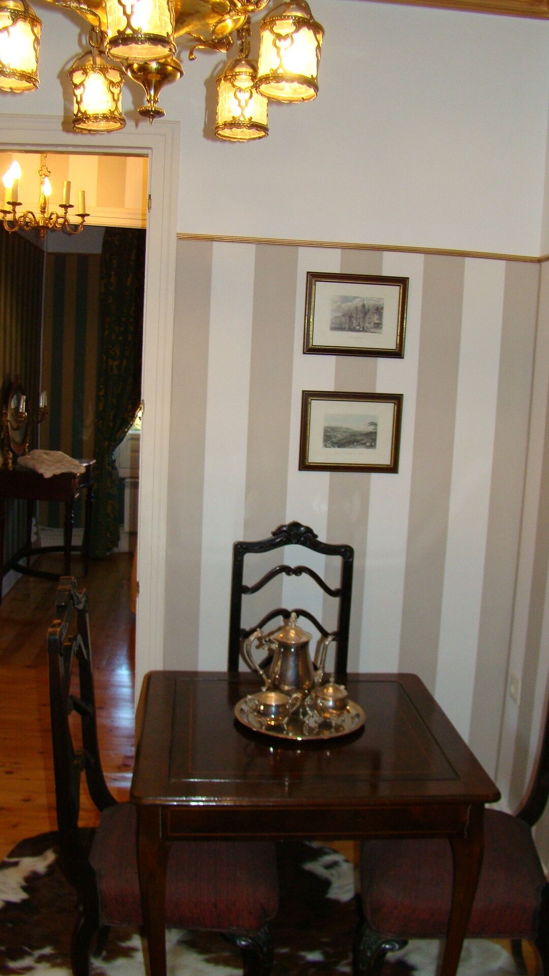 Un comedor con una mesa de madera, una bandeja de metal con una jarrón y dos cuadros en la pared.