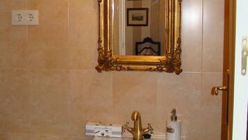 Een badkamer met een spiegel met gouden lijst, een wit wastafelmeubel met gouden kraan, en een wit toilet.