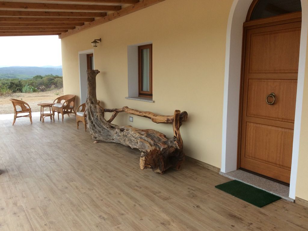 A wooden bench and chairs outside a building with a wooden door and a window.
