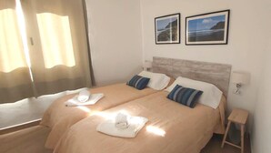 Cama doble con dos almohadas, una mesita de noche y dos cuadros enmarcados en la pared.