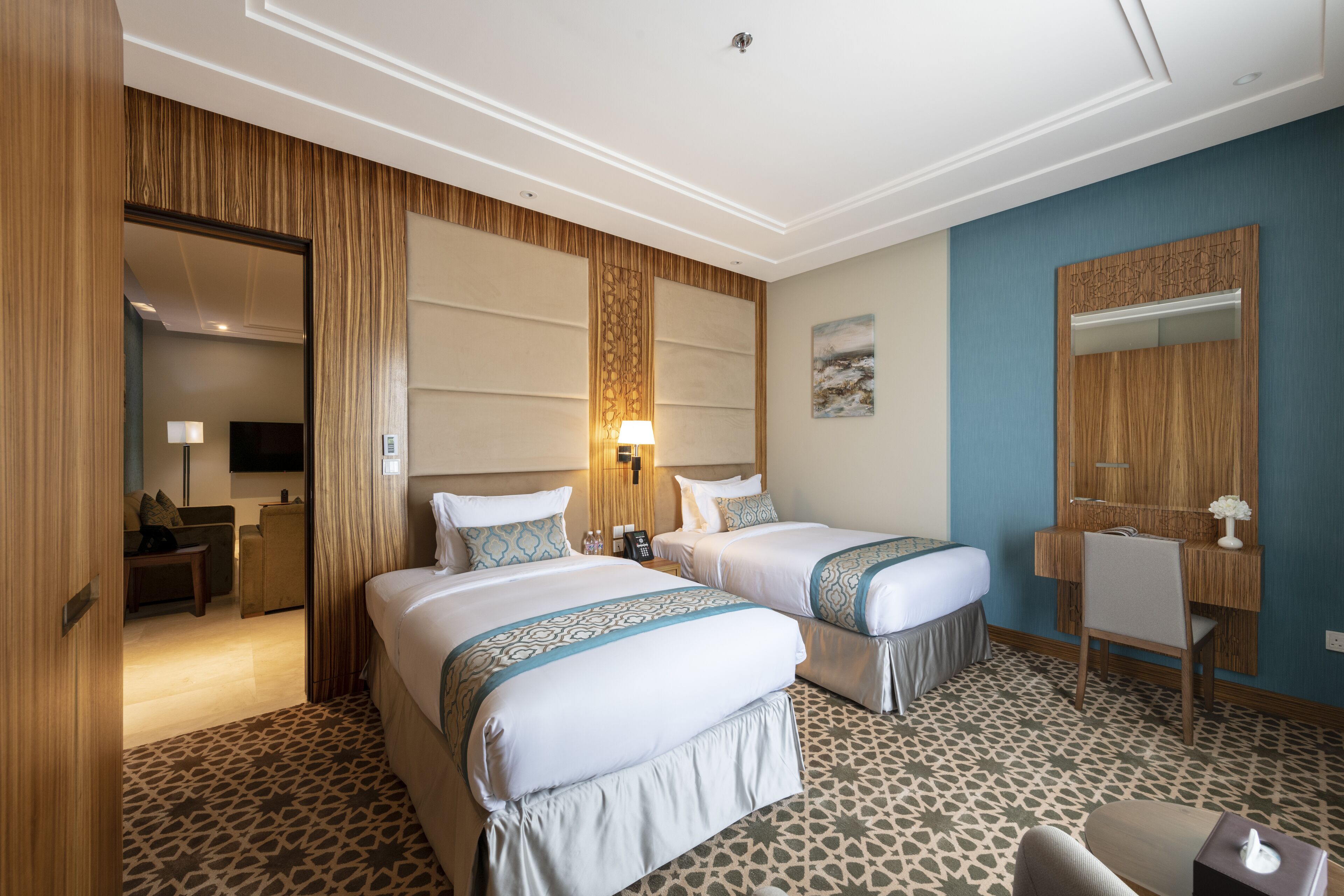 A hotel room with two beds, a desk, a chair, a mirror, and a patterned floor.