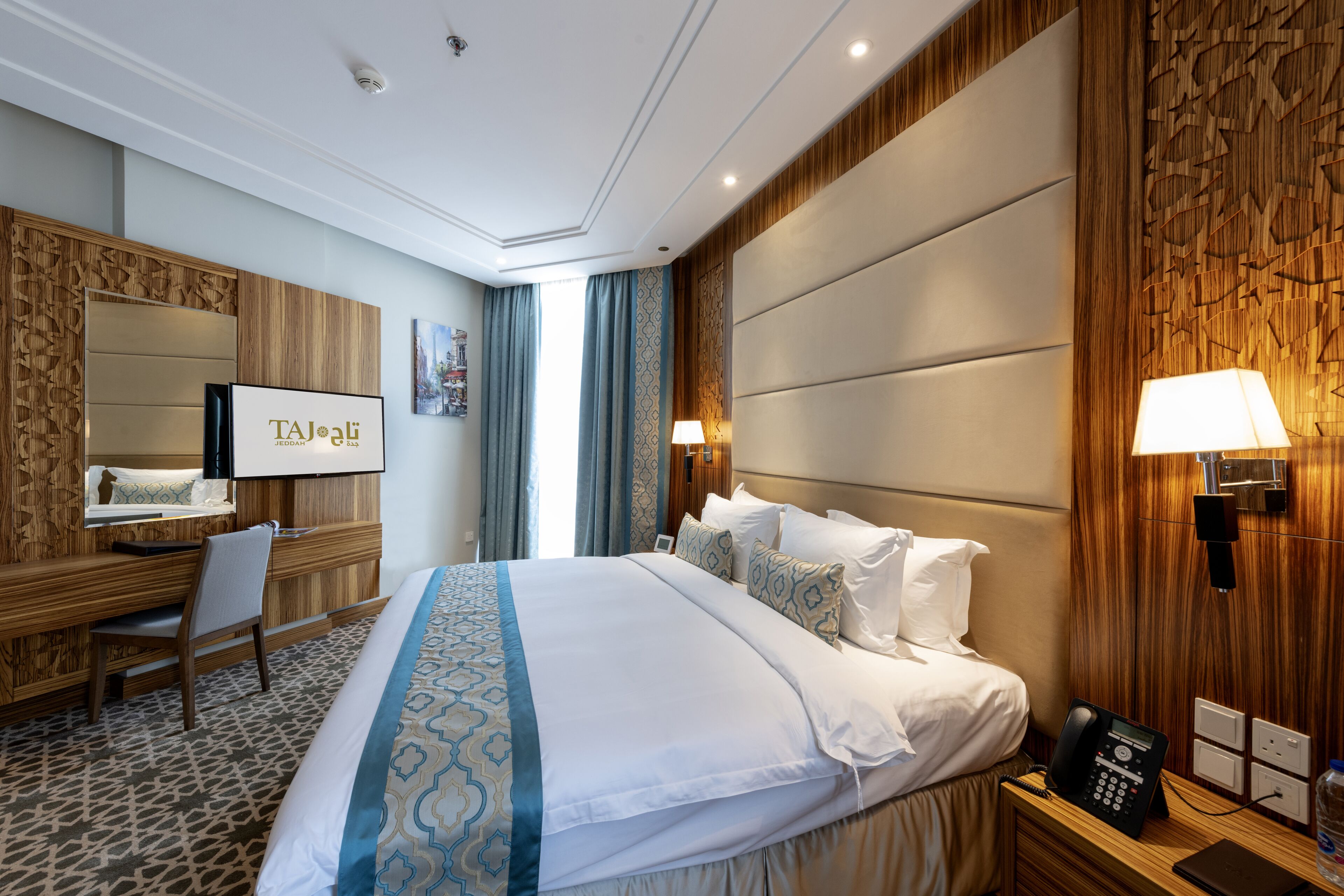 Een hotelkamer met een groot bed, een bureau met stoel, een spiegel en een aan de muur bevestigd telefoon.
