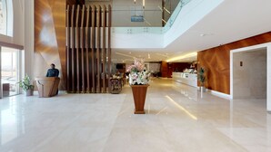 A spacious lobby with a reception desk, a large floral arrangement, and a modern staircase.