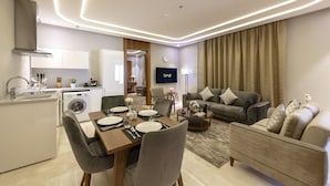 A modern living room with a sofa, a dining table set for four, and a kitchen area with a washing machine.