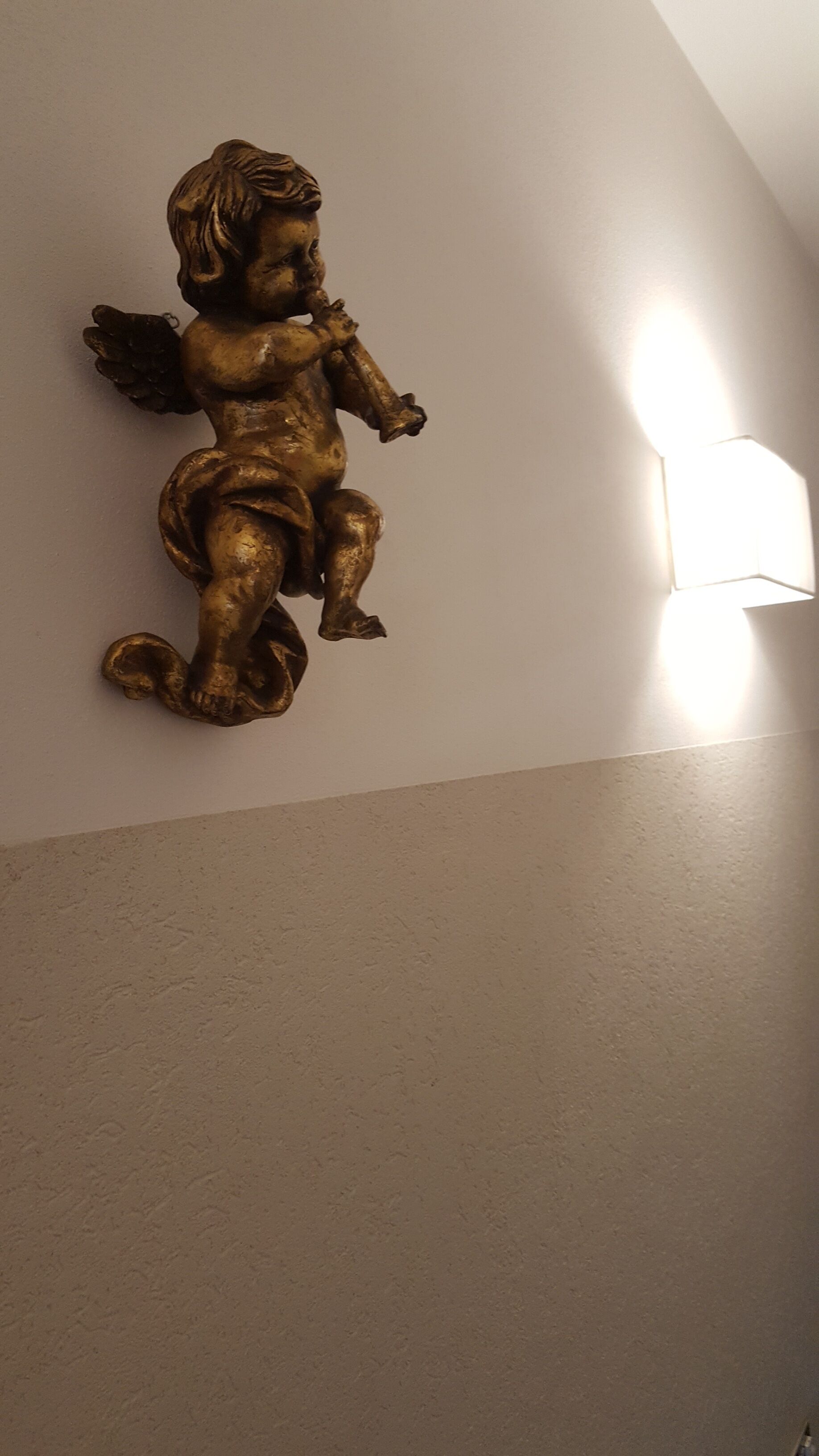 A wall-mounted golden angel sculpture with a light fixture to its right.