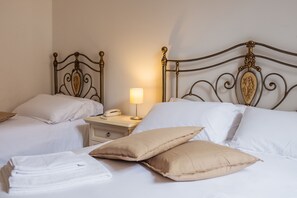 A hotel room with two beds, each with white bedding and a decorative headboard. There is a bedside table with a lamp and a telephone. - Hotel Panorama (Bertinoro)