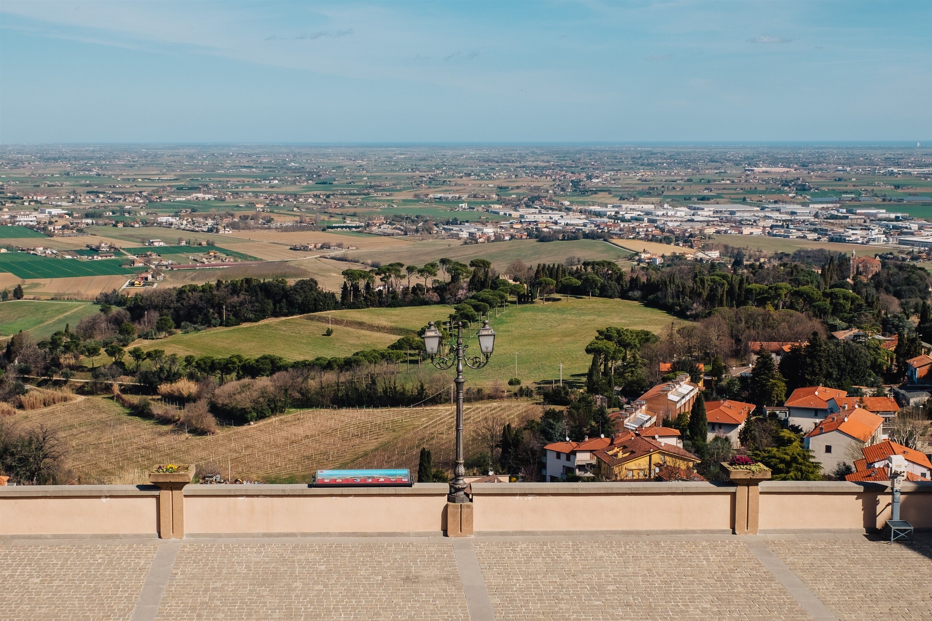 A panoramic view of a town with a prominent hill, a train track, and a street lamp in the foreground.