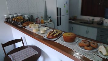 Una cocina con mostrador que exhibe varios productos horneados, un refrigerador y un comedor con una silla y una mesa.