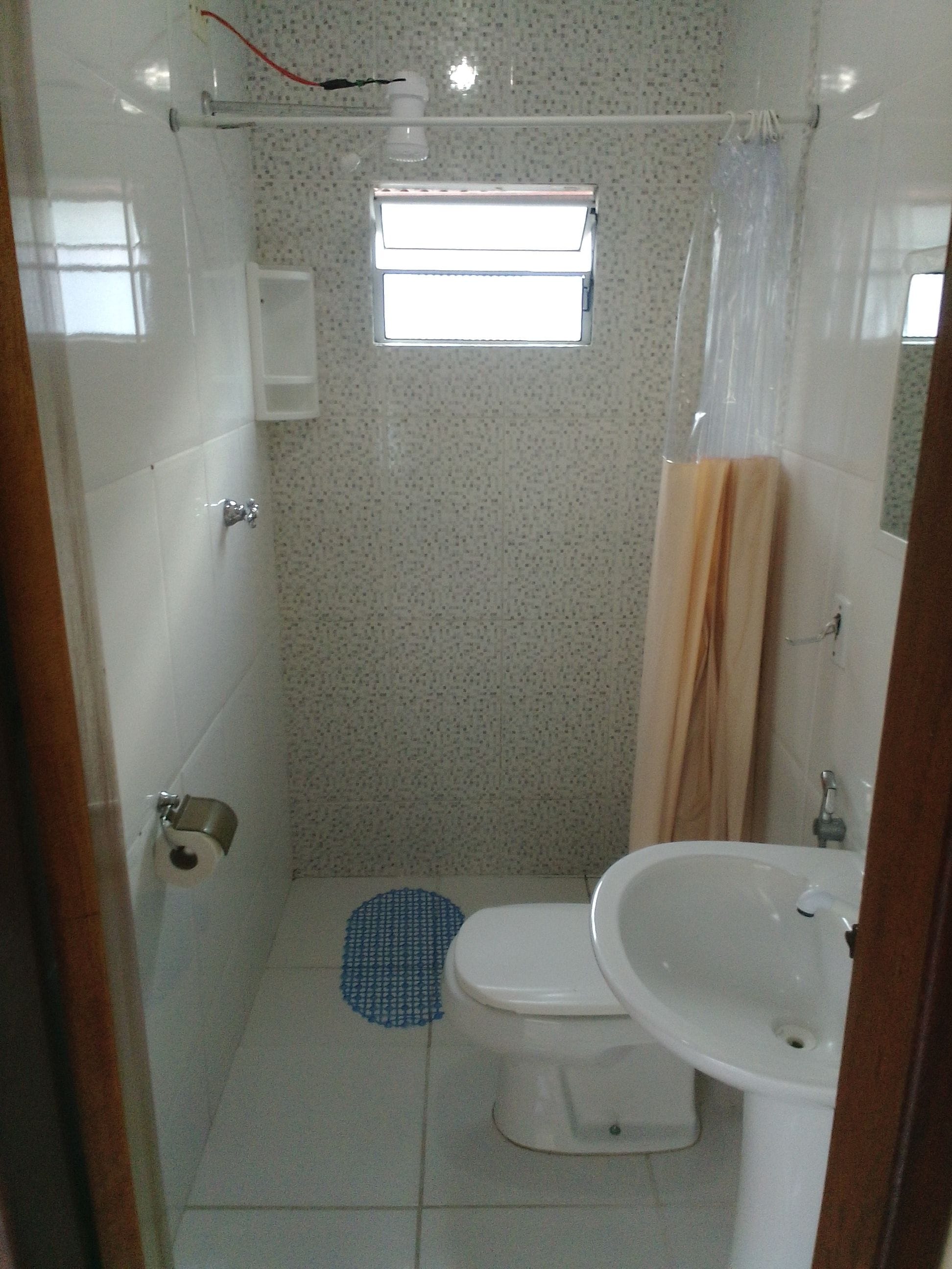 A bathroom with a toilet, sink, shower, and a small window.