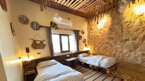 A room with two beds, a wooden headboard, a stone wall, and a window with curtains. - Carob Hostel (Amman)