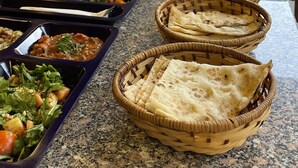 A buffet with various food items and baskets of flatbread. - Carob Hostel (Amman)