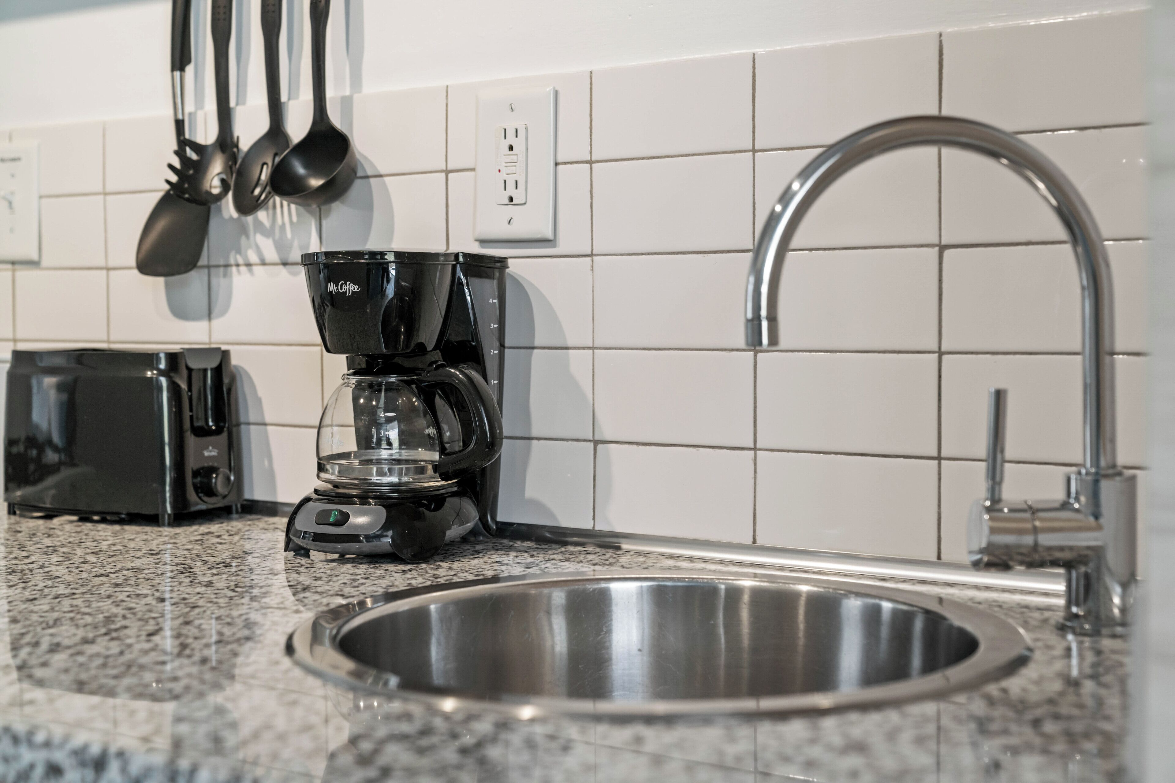 A kitchen with a stainless steel sink, a coffee maker, and a toaster.
