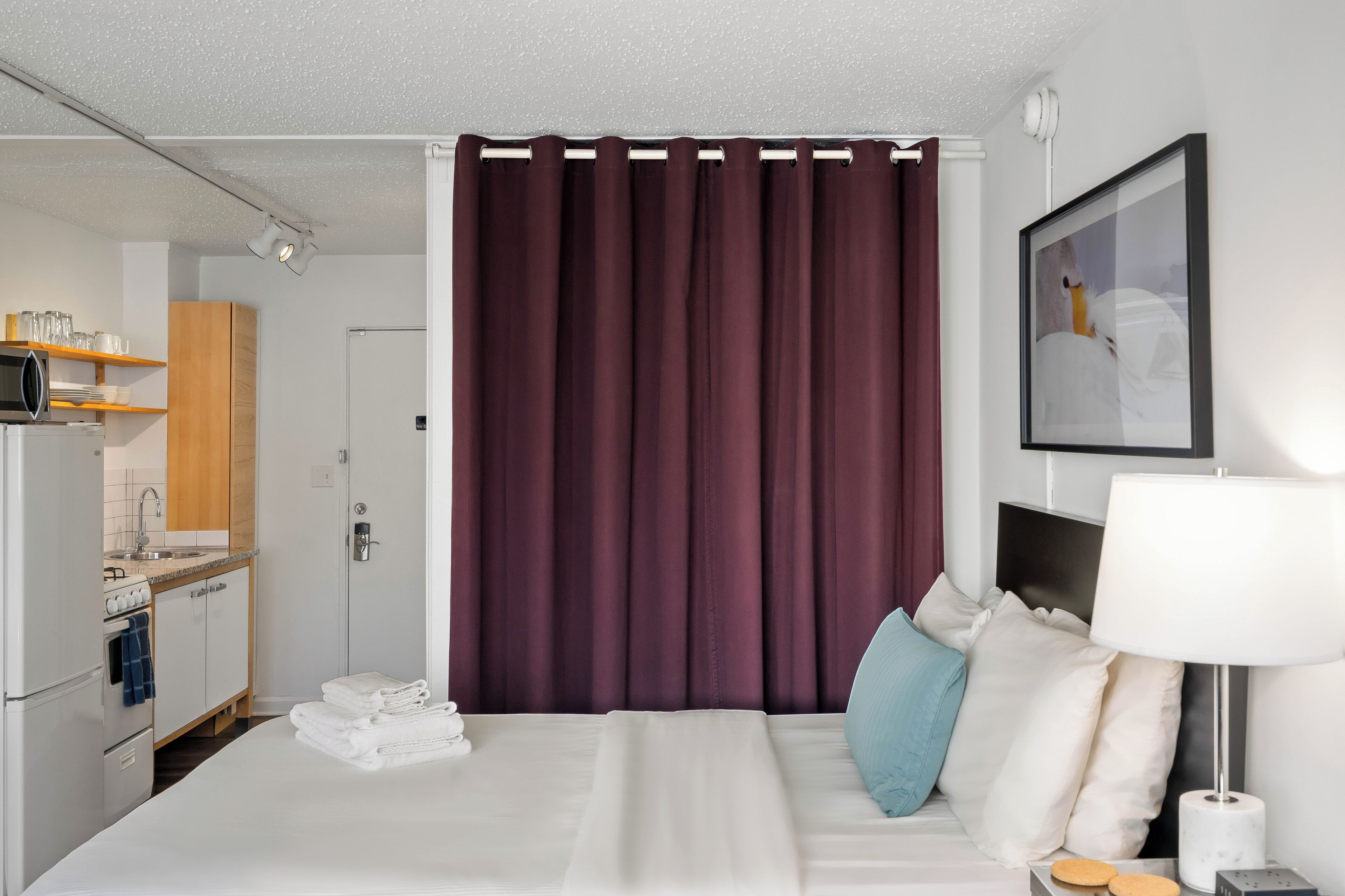 Ein Hotelzimmer mit Bett, Schreibtisch, Stuhl, Lampe, einem Bild an der Wand und einem Vorhang.