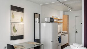 A compact hotel room with a kitchenette, a dining area with a table and chairs, and artwork on the wall.