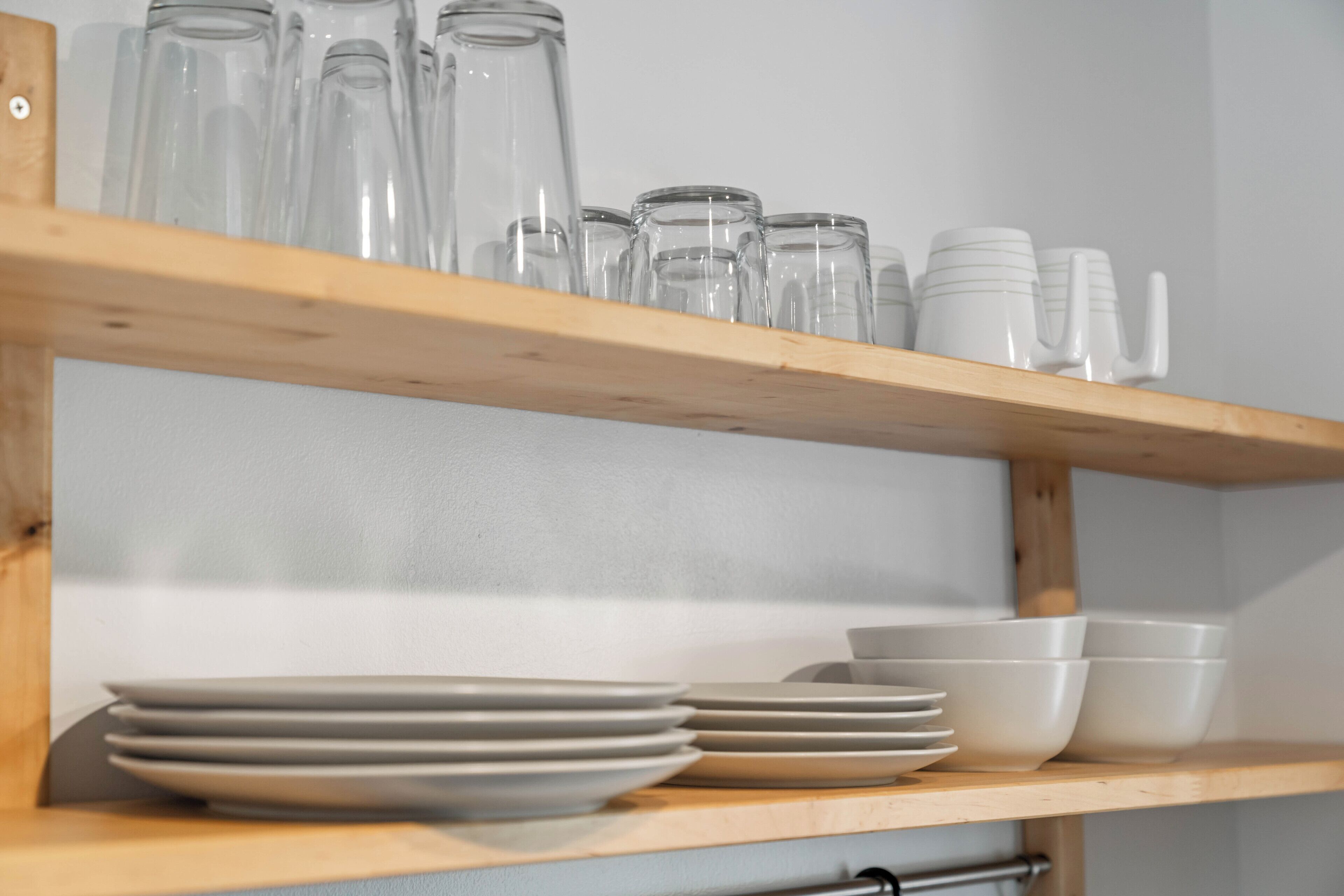 A wooden shelf with clear glass bottles and white ceramic plates and bowls.