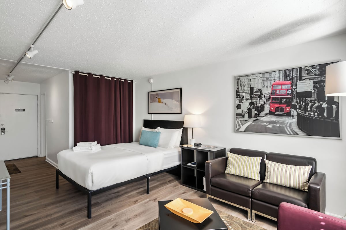 A hotel room with a bed, a desk, a sofa, and a painting of a red bus.