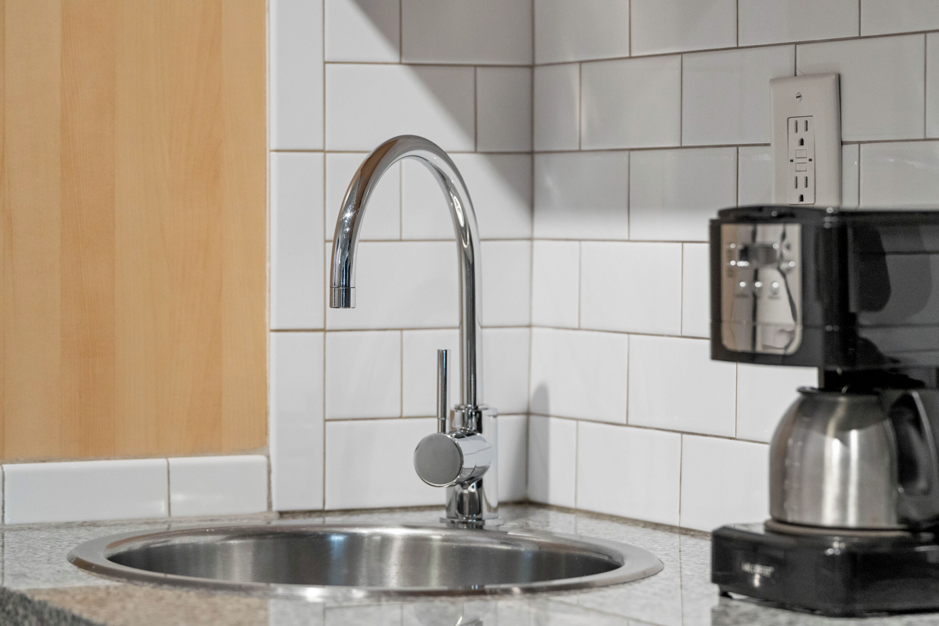 Una cocina con un lavamanos de acero inoxidable, un grifo moderno y una cafetera sobre la encimera.