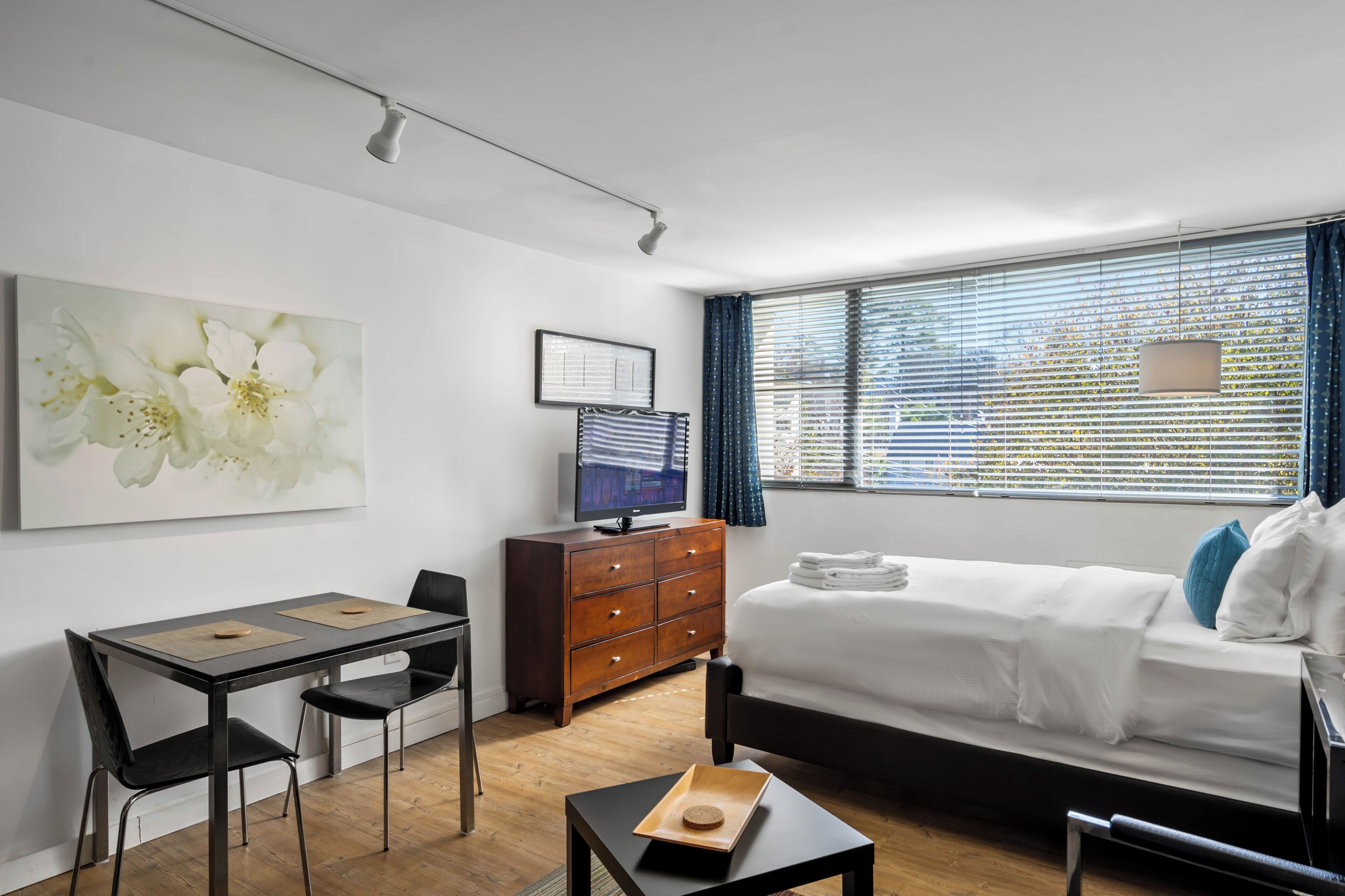 Une chambre d’hôtel moderne équipée d’un lit, d’un bureau avec deux chaises, d’une télévision et d’une grande fenêtre avec des stores.