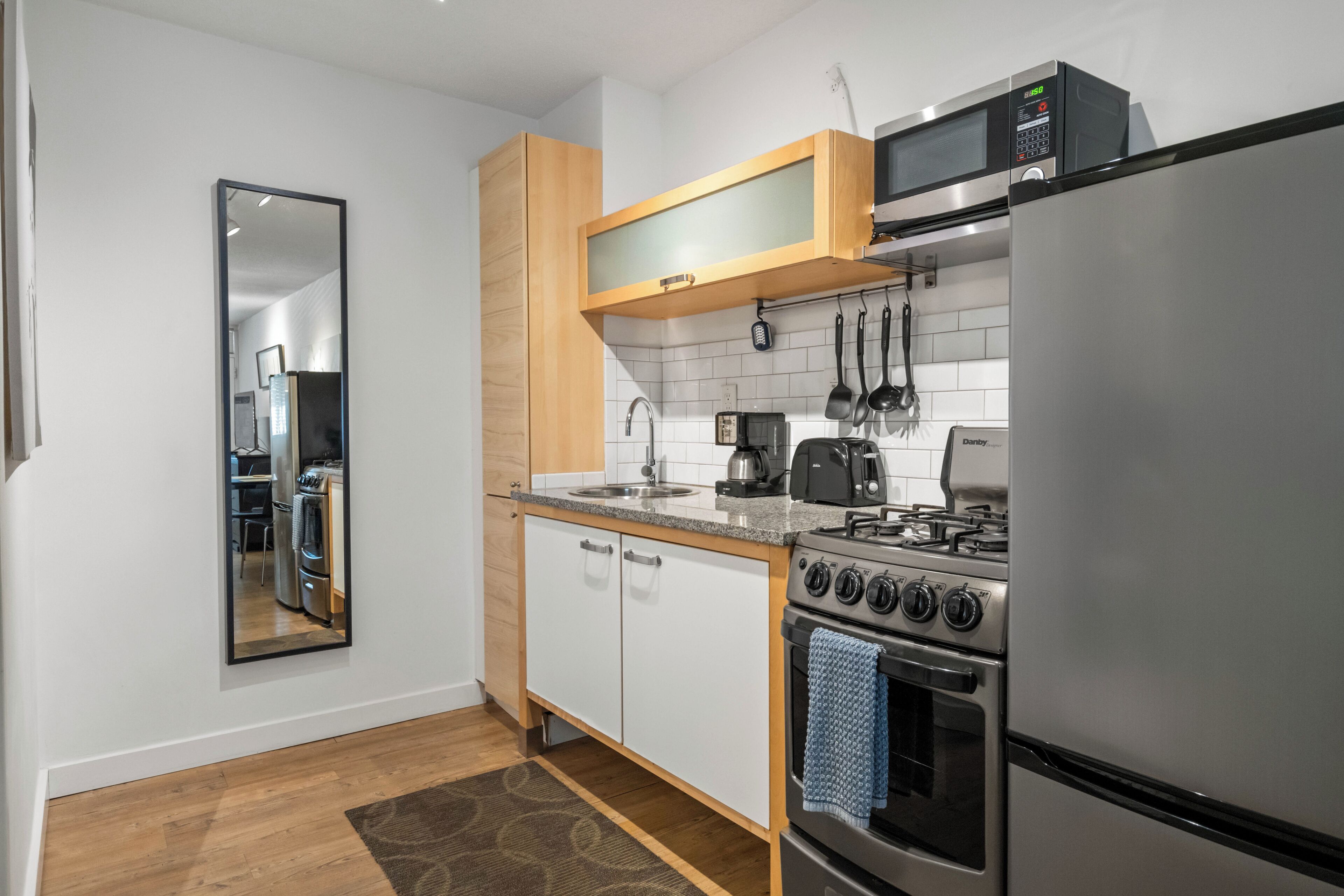 A compact kitchen with white cabinets, a stainless steel refrigerator, a microwave, a stove, and a coffee maker.