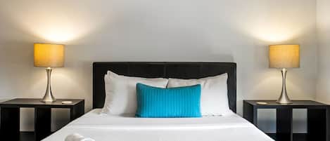 A neatly made bed with white linens and a blue pillow, flanked by two black nightstands with lamps.