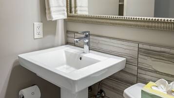 Une salle de bain avec un lavabo blanc, un miroir doté d’un cadre décoratif, un porte-serviettes et des toilettes avec un présentoir à mouchoirs.