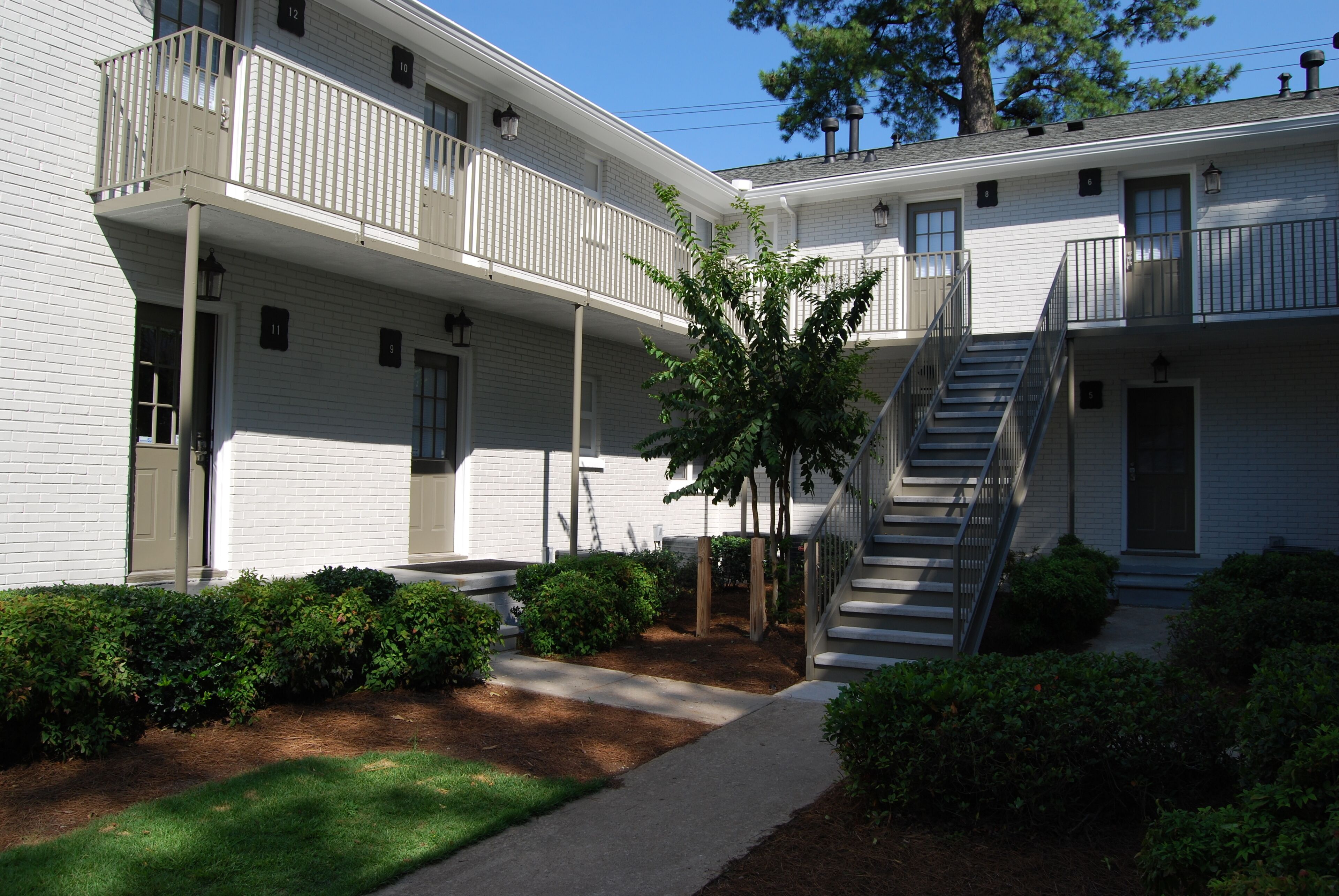 A two-story building with a central courtyard, a staircase, and a small tree.