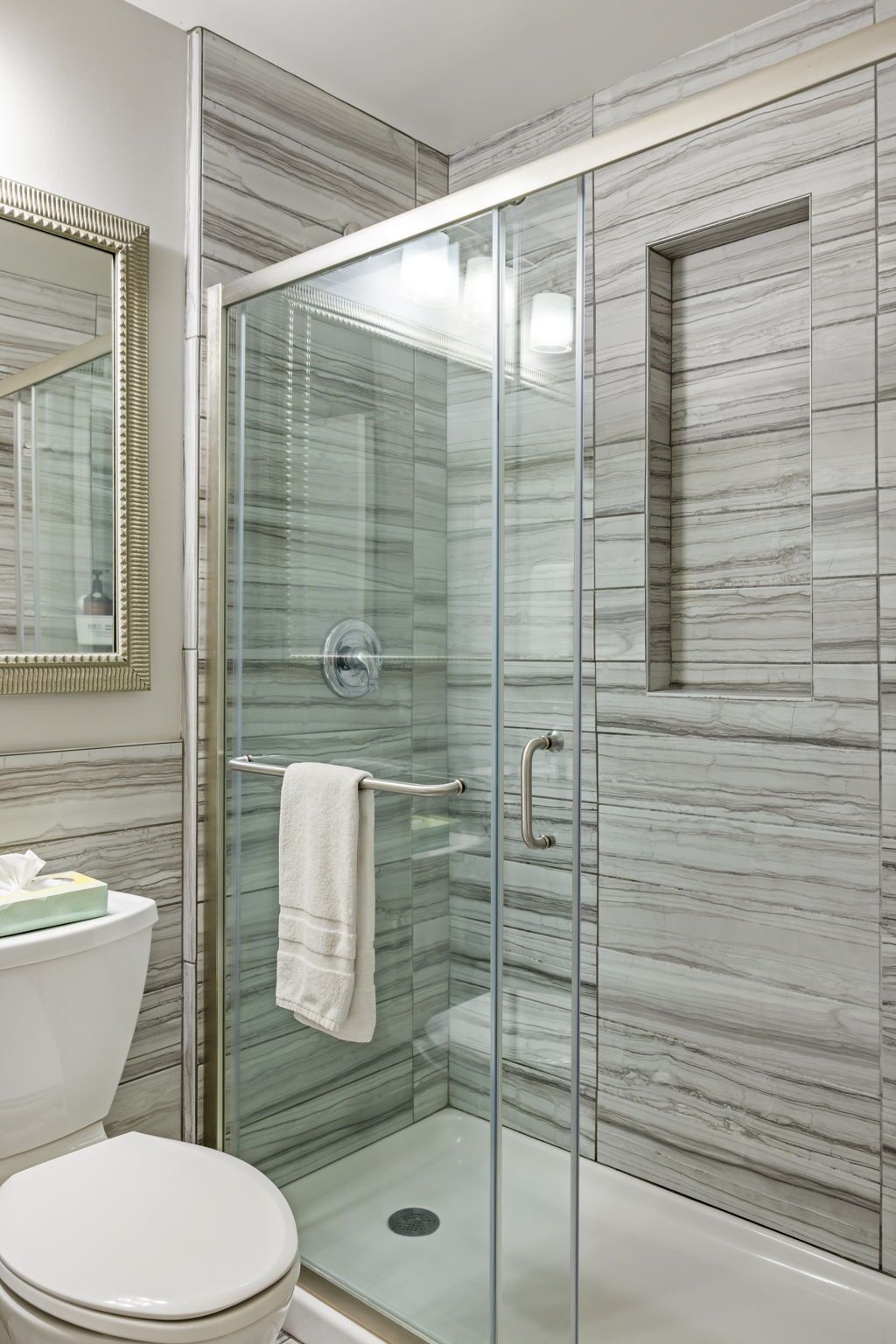 Une salle de bain moderne avec une douche à parois de verre, des murs en marbre, des toilettes et un grand miroir.