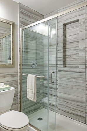 A modern bathroom with a glass-enclosed shower, marble walls, a toilet, and a large mirror.