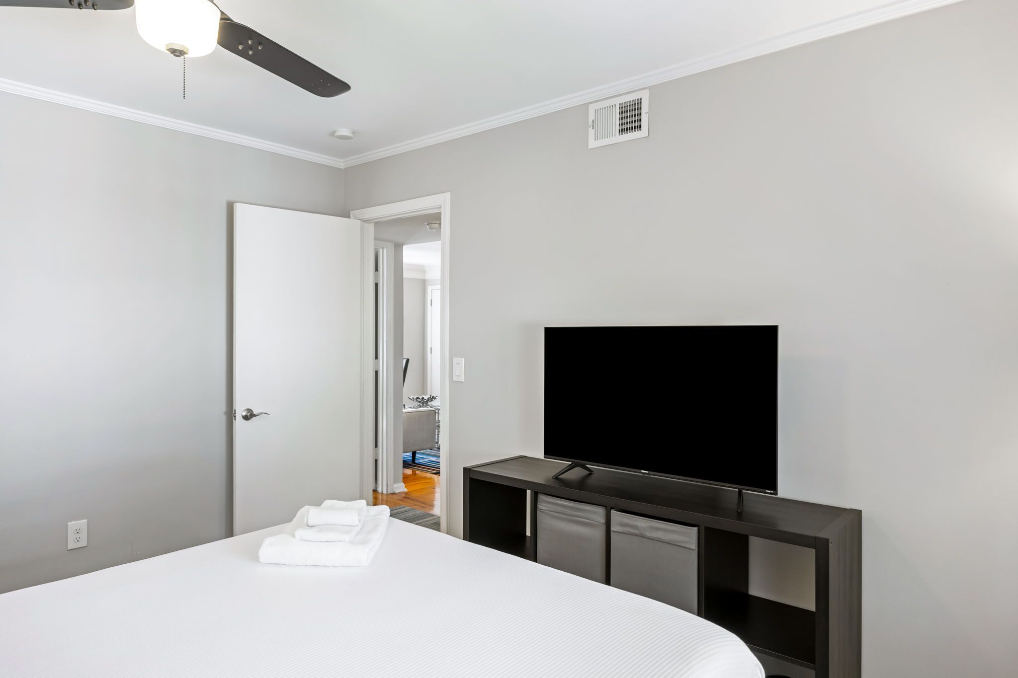 A hotel room with a bed, a flat-screen TV, a ceiling fan, and a door leading to a bathroom.