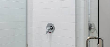 Una ducha moderna con puerta de vidrio, cabezal de ducha de mano y grifo empotrado.