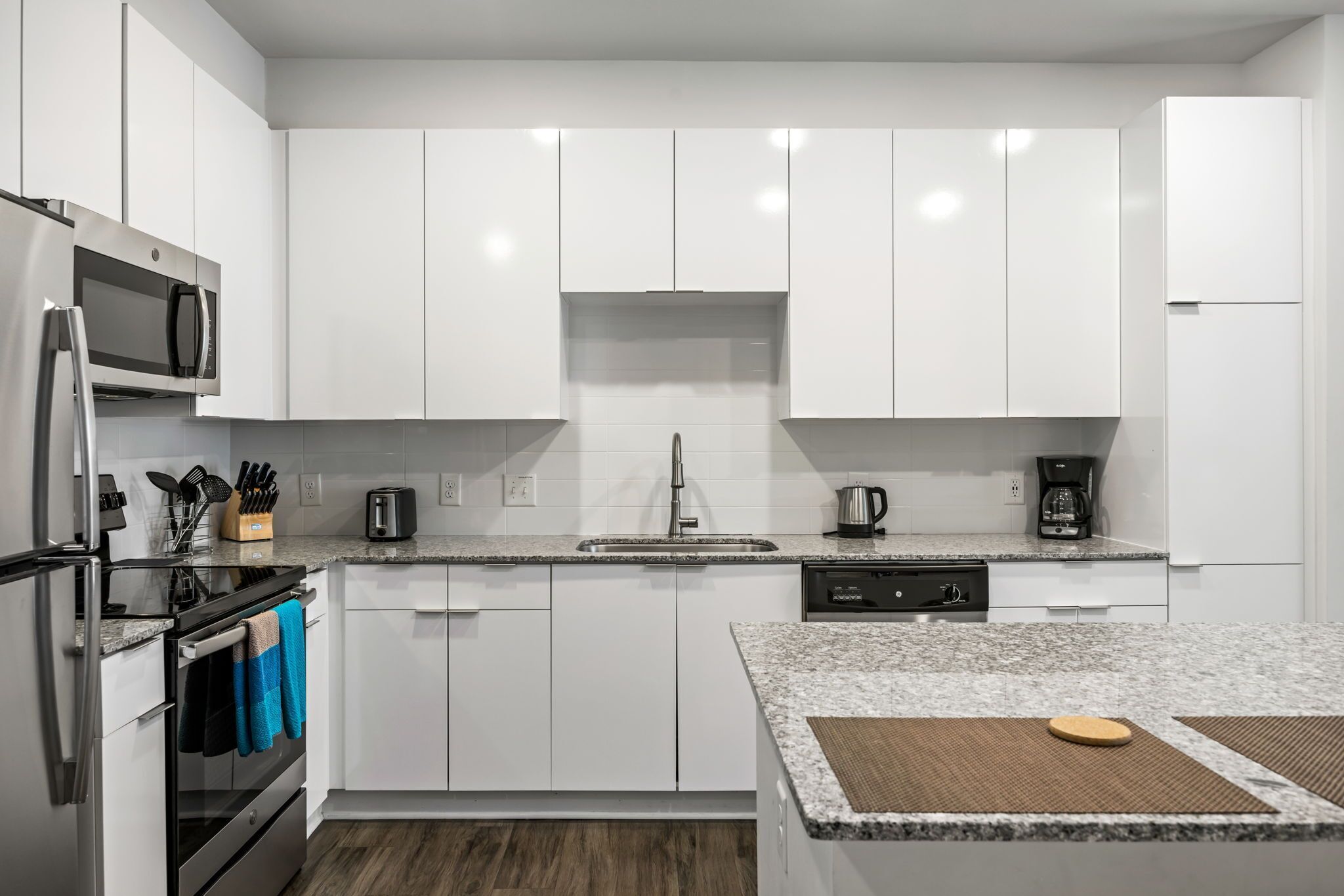 A modern kitchen with white cabinets, stainless steel appliances, a granite countertop, and a wooden floor.
