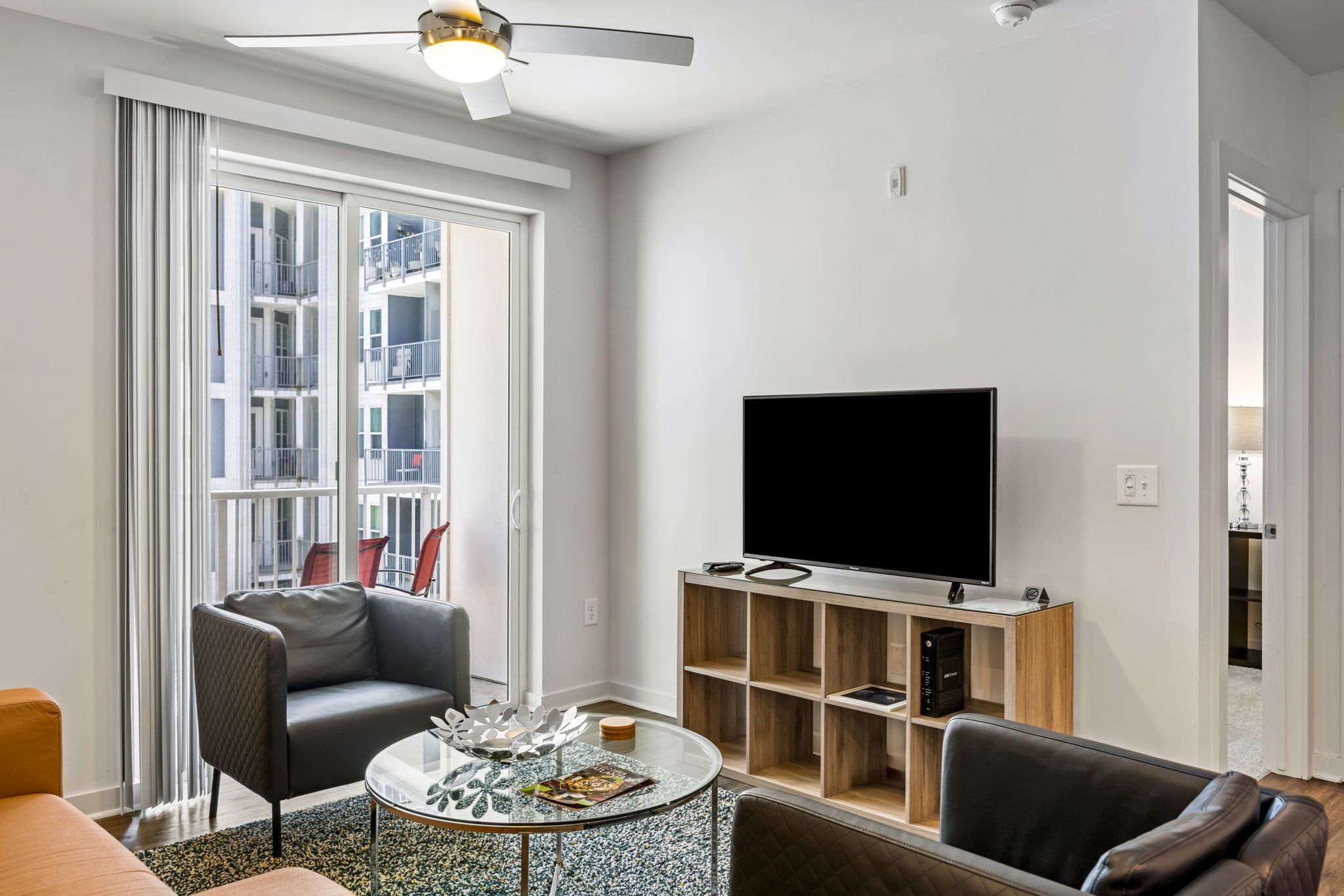 A modern living room with a large TV, comfortable seating, and a balcony with a view.