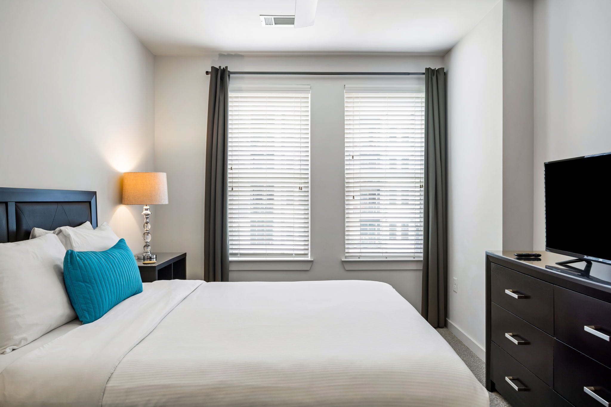 Une chambre d’hôtel comprenant un lit, une table de chevet avec une lampe, une commode et un téléviseur.