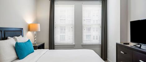 Une chambre d’hôtel comprenant un lit, une table de chevet avec une lampe, une commode et un téléviseur.