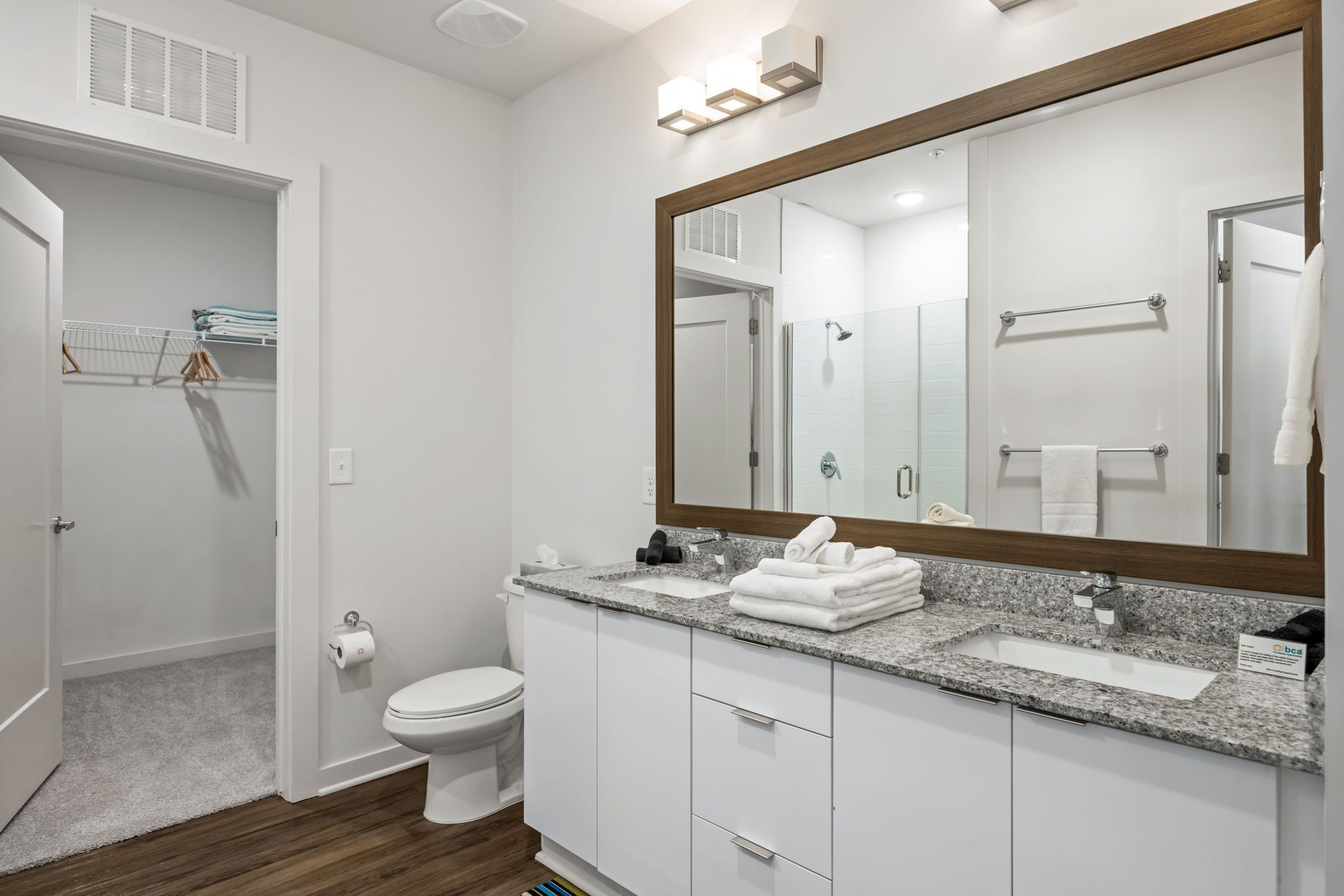A modern bathroom with a large mirror, white cabinets, a granite countertop, and a shower area.