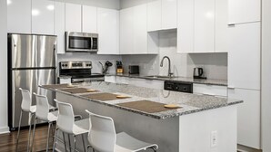Una cocina moderna con gabinetes blancos, electrodomésticos de acero inoxidable, encimera de granito y taburetes de bar.