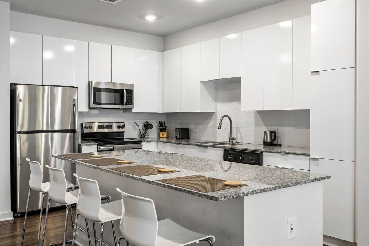 A modern kitchen with white cabinets, stainless steel appliances, a granite countertop, and bar stools.