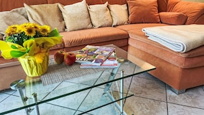 Ein modernes Wohnzimmer mit einem braunen Sofa, einem Glastisch, einem Strauß Sonnenblumen, zwei Äpfeln und einer Zeitschrift.